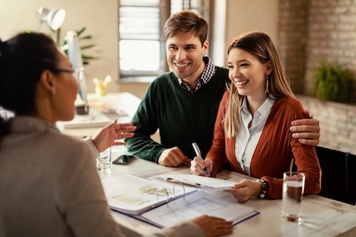 Happy couple signing mortgage contract while having meeting with real estate agent